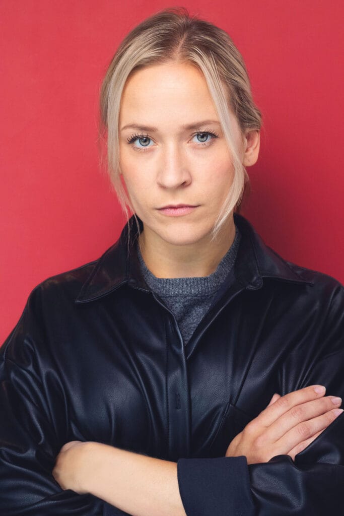 Actress, blonde with black leather jacket, crossing her arms, powerful, not approachable, red backdrop, nyc headshot backdrop