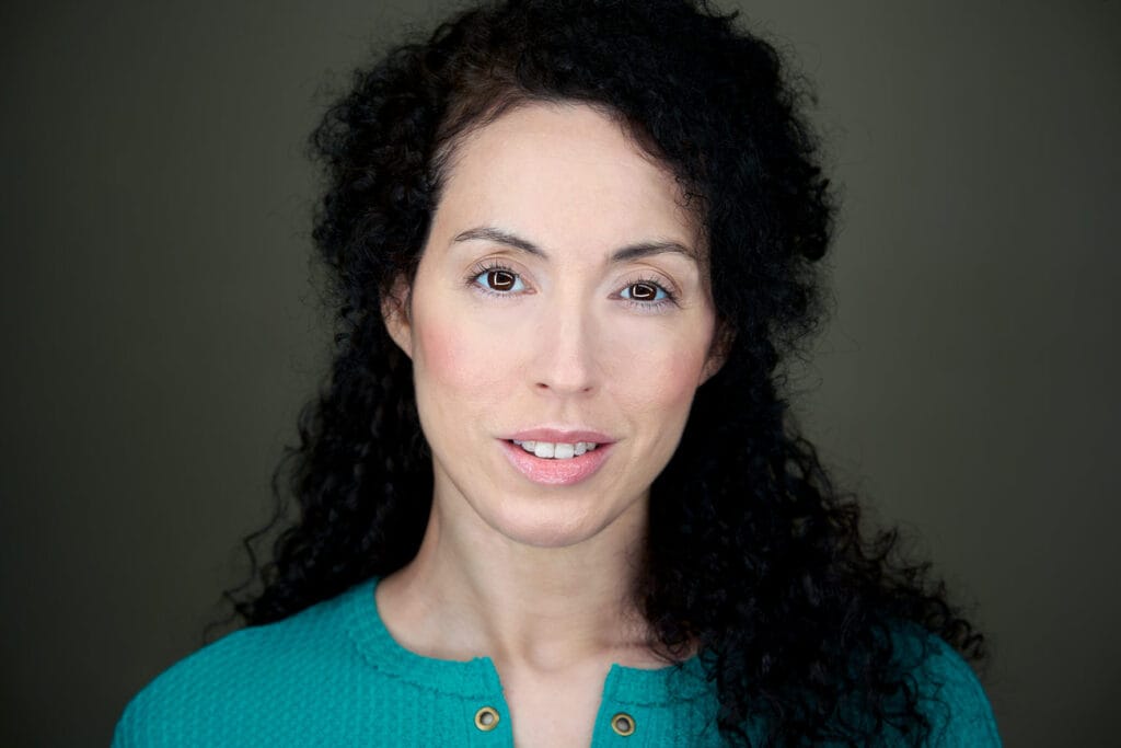 Brunette with curly hair, teal shirt, wonderful gaze to the camera, gray backdrop, nyc headshot photographer