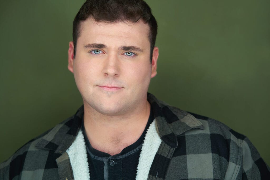 Male actor with flannel like jacket, black henley, broad shoulders, blue/gray eyes, green backdrop, smoldering to the camera, actor, headshot, nyc actor headshot, nyc photorapher