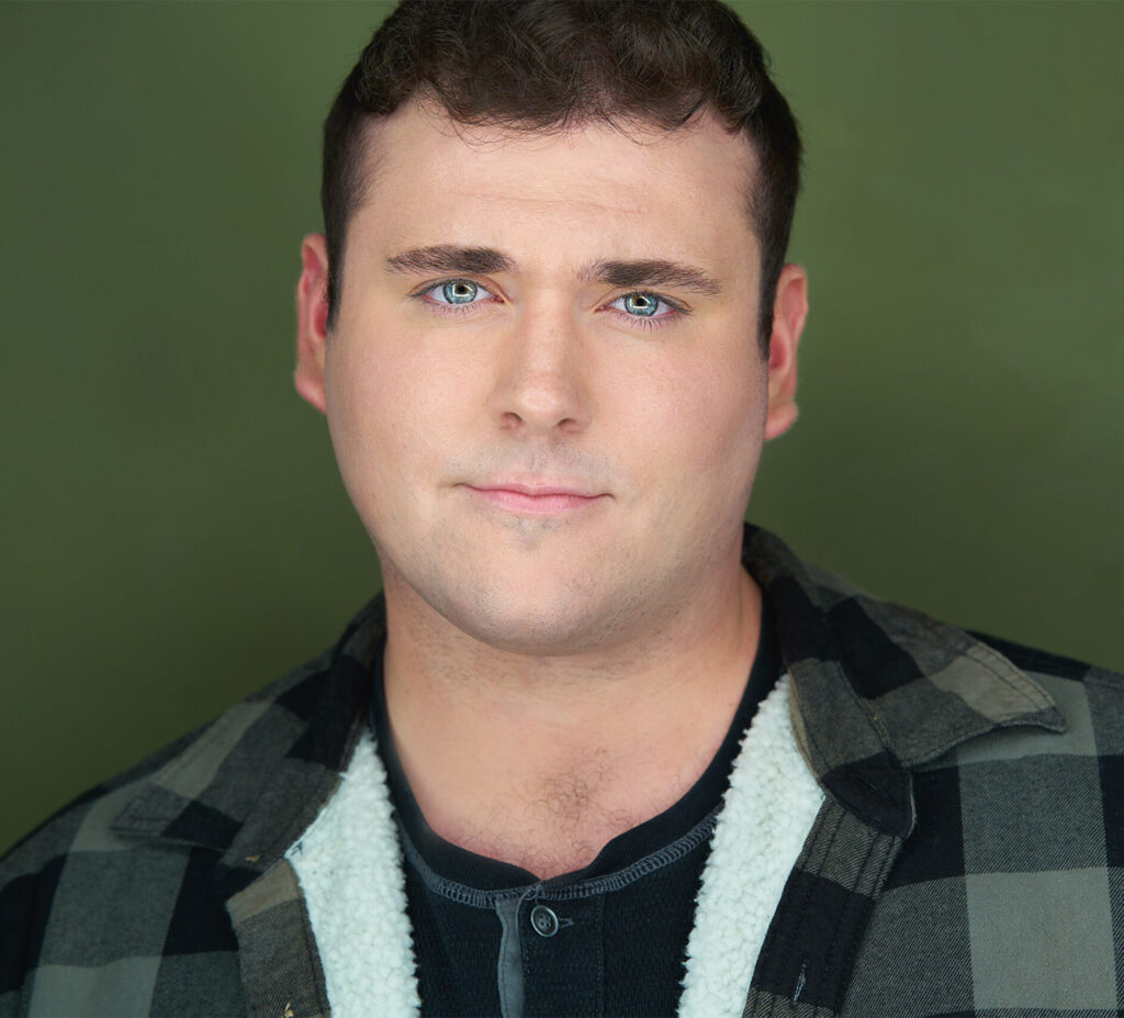 Male actor with flannel like jacket, black henley, broad shoulders, blue/gray eyes, green backdrop, smoldering to the camera, actor, headshot, nyc actor headshot, nyc photorapher