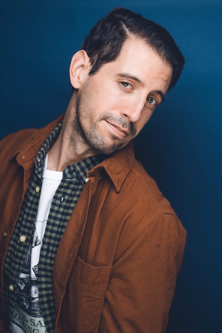 Portrait of Jonathan Vane, quirky and fun, against a blue background with an intriguing expression.