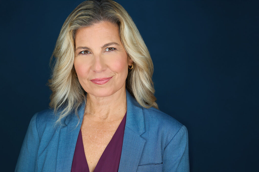 Blonde woman, headshot, blue jacket, purple blouse, blue backdrop, approachable closed mouth smile, nyc photographer