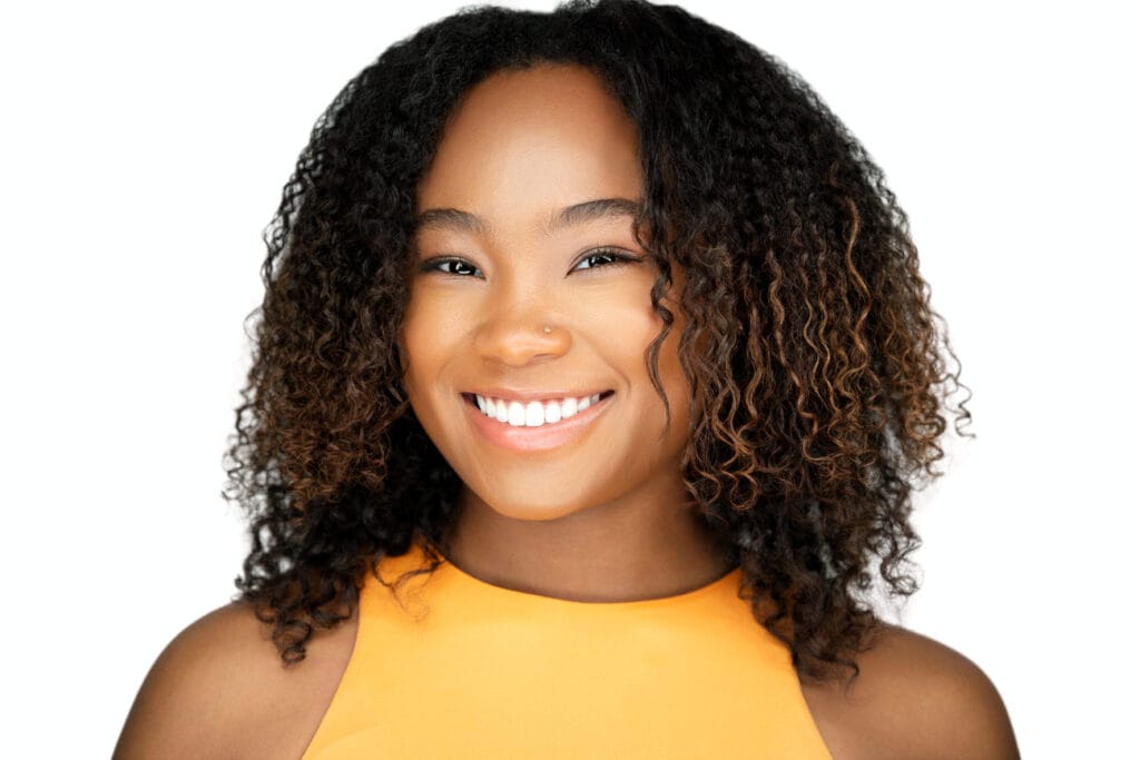 Black young lady with bright smile, yellow top, puffy hair, white backdrop, approachable and vibrant, nyc headshot photographer