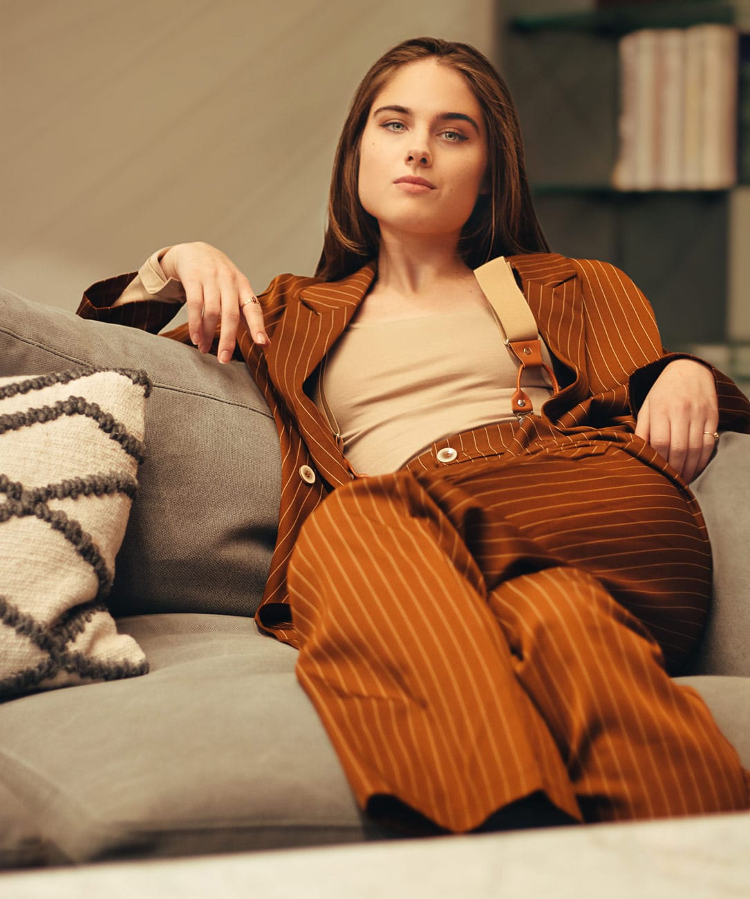 Gorgeous model in a power business suit leaning back on a couch, exuding fierceness and sophistication.