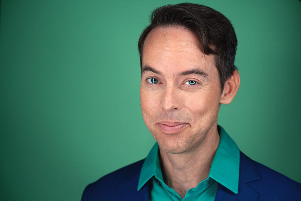 Actor with fun, approachable smirk, green button down, with navy blue jacket, mint green backdrop, nyc photographer