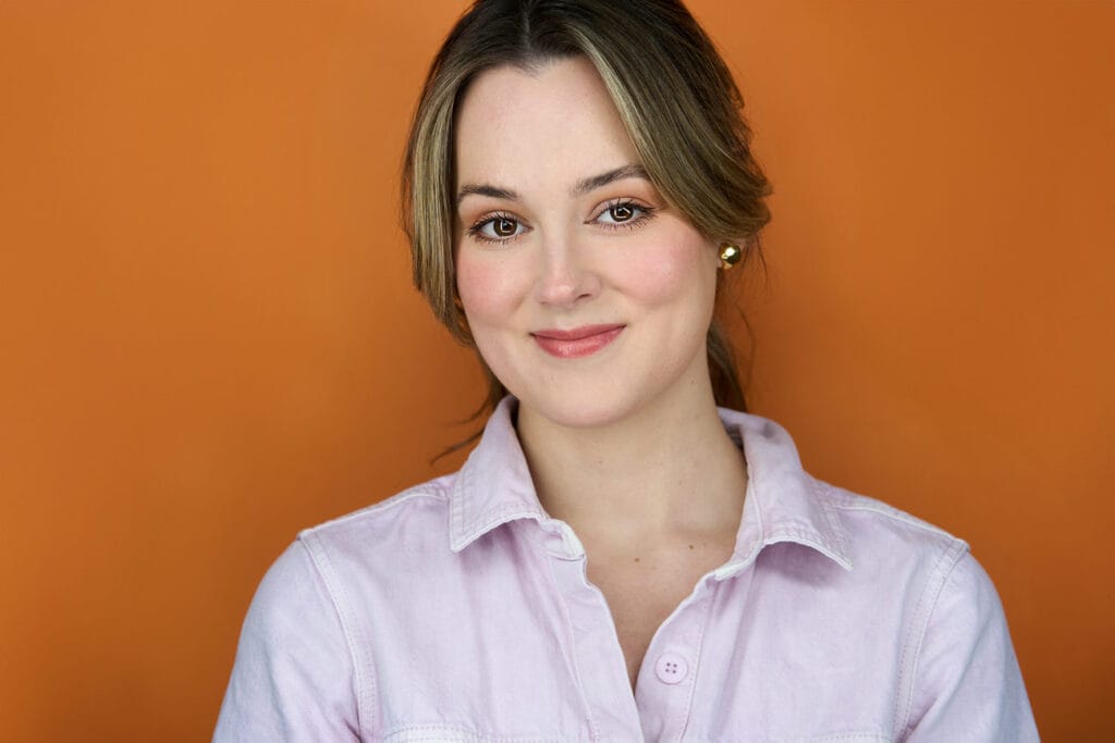 Actress, headshot, no teeth smile, pink jumpsuit, chest high shot, orange backdrop, nyc photographer