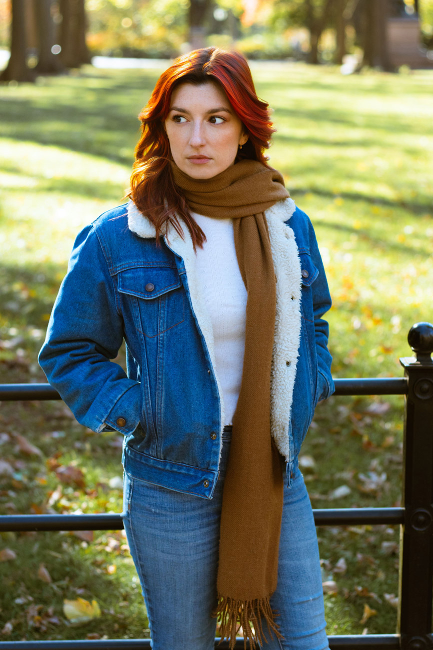 Woman in a jean jacket, jeans, and scarf looking away from the camera in Central Park. Portrait photography.