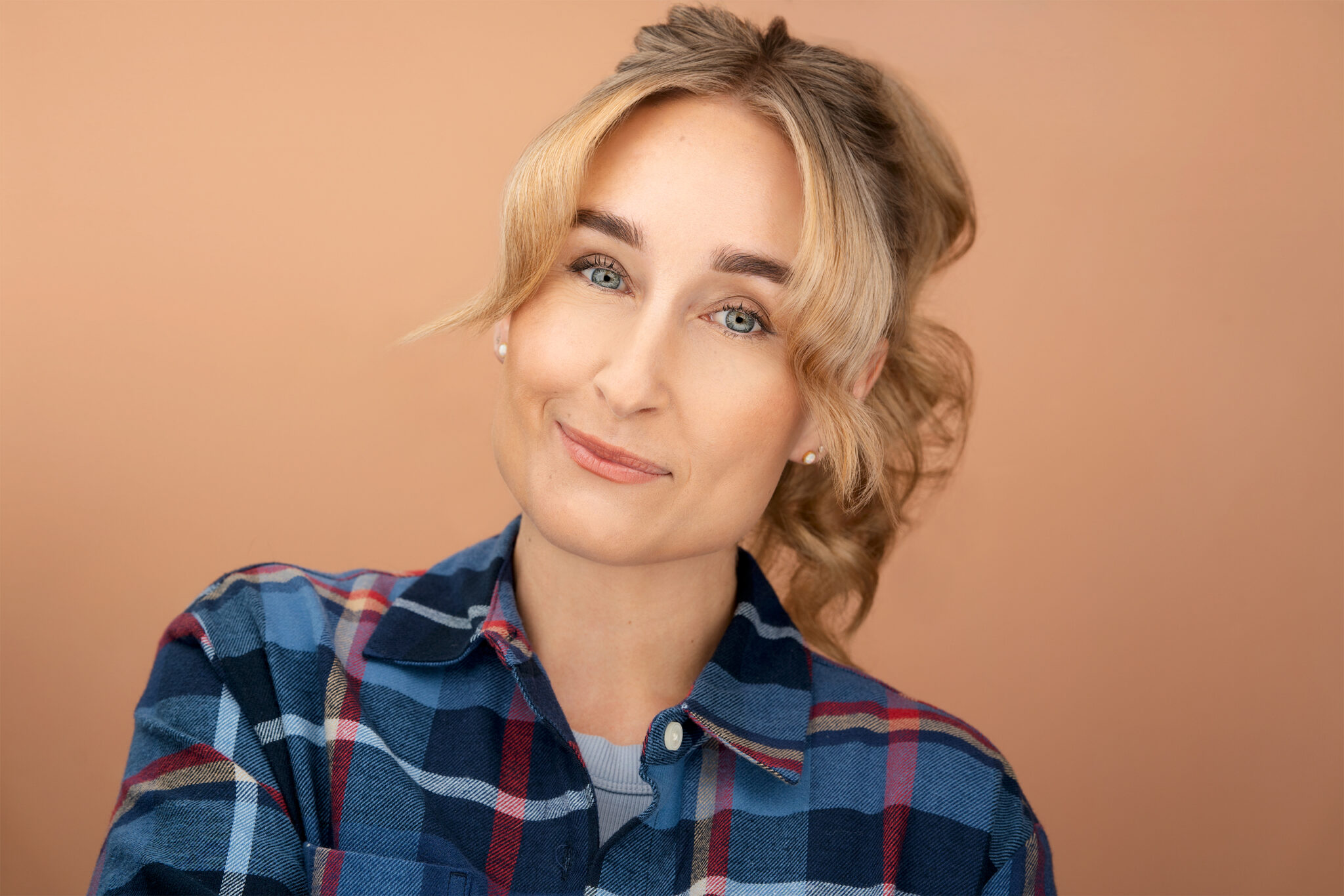 blone, blue eye woman, with flannel shirt, actress, headshot, peach backdrop, slight smile, nyc