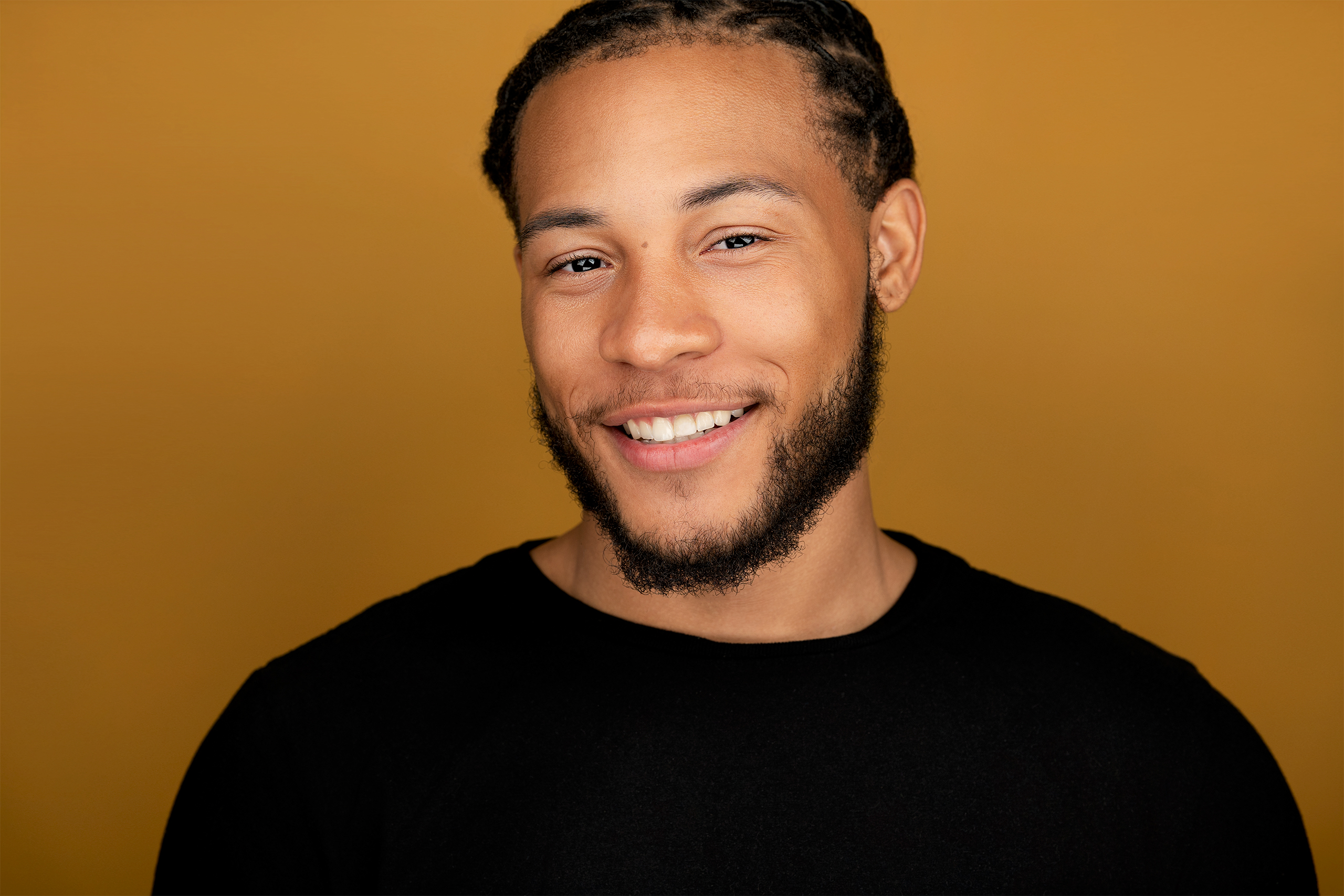 Man with smoldering gaze, half smile, black shirt, brown backdrop, actor, headshot, nyc