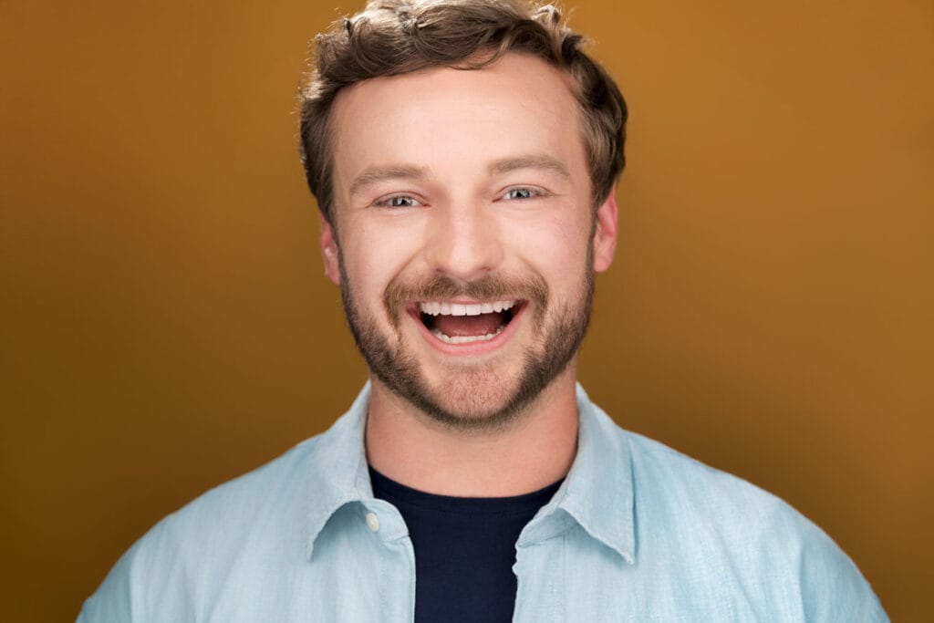 actor with bear laughing/smiling wide open staring at the camera - orange/brown backdrop