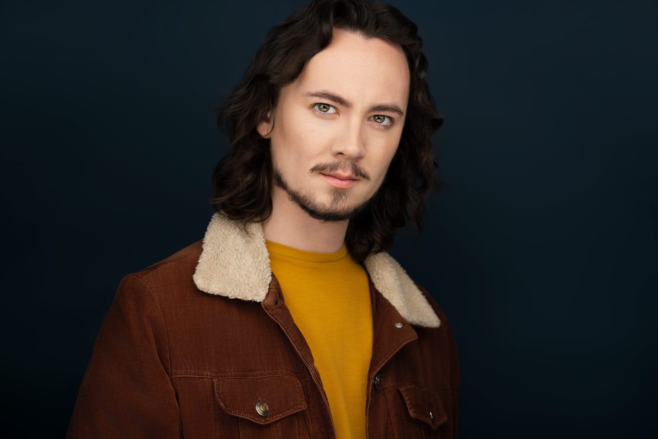 Actor with a piercing gaze, mustache and goatee, wearing a mustard shirt, brown corderoy jacket, long brown hair - NYC Headshot Photographer