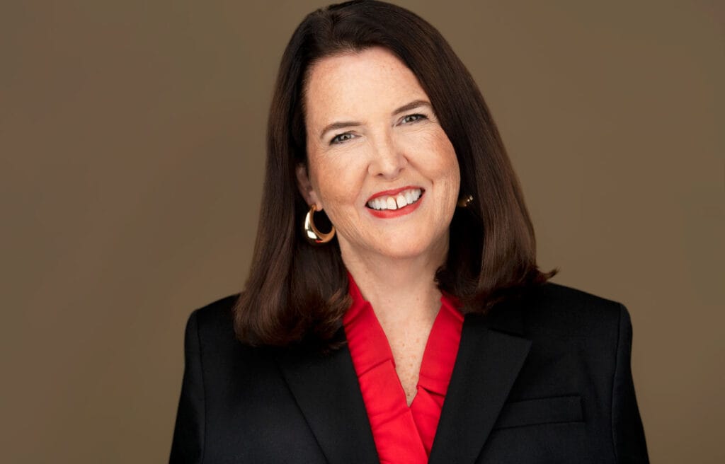 Business professional with a genuine kind smile - red blouse and black business jacket with brown hair to her shoulders - Headshot NYC Photographer