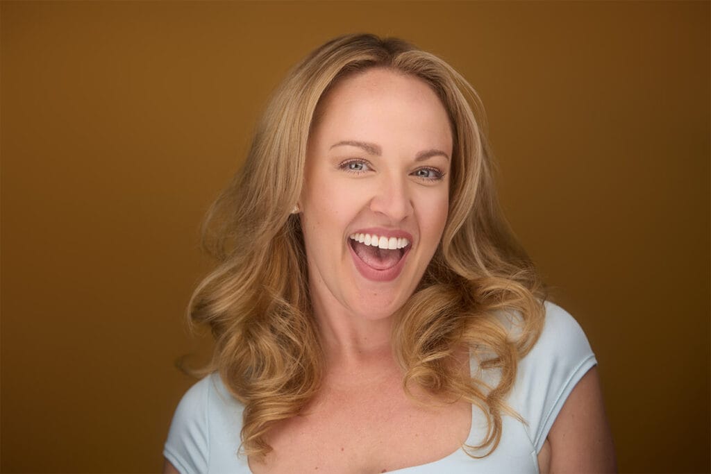 Fun, blonde girl, with great personality, teal blue top, brown backdrop, smiling, laughing, happy all at once. NYC Headshot Photographer