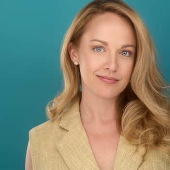Blonde, blue eye lady, with beige top, teal backdrop, sly smile, approachable, NYC Photographer