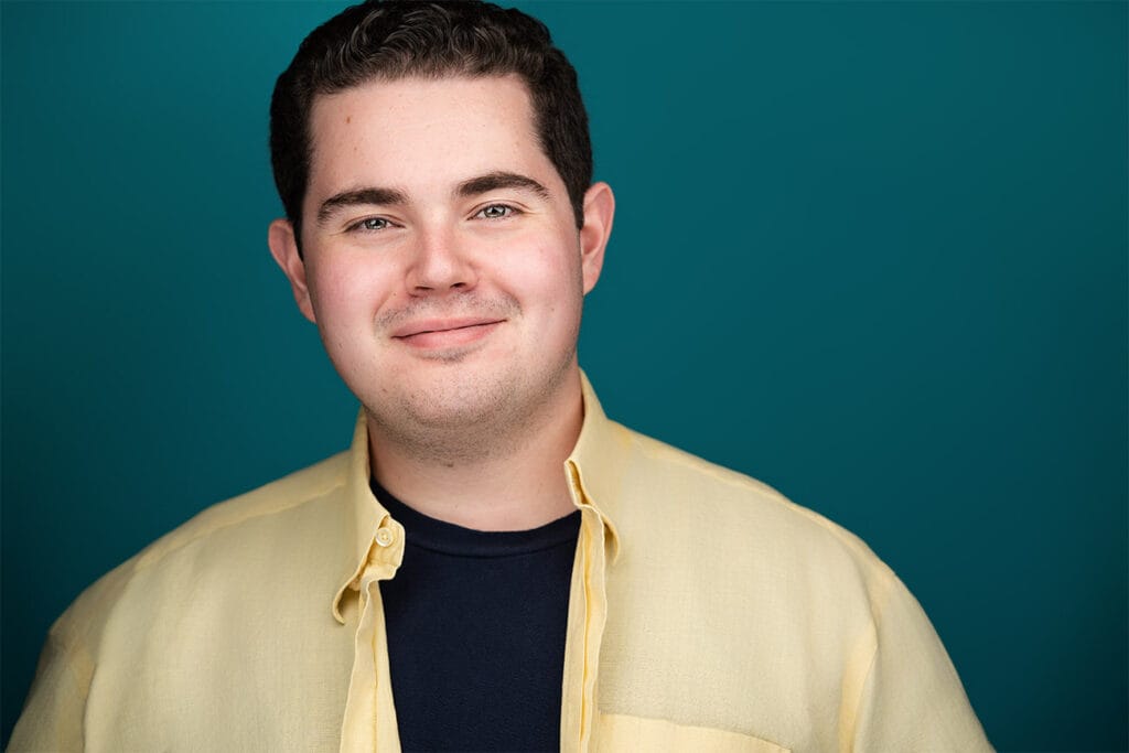 Crisp smile of gentleman with yellow button down shirt opened, blue under shirt, teal backdrop, headshot, nyc headshot photographer