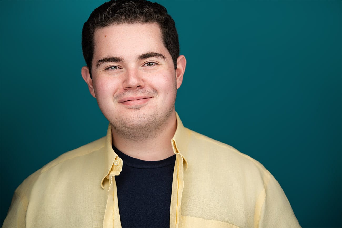 Crisp smile of gentleman with yellow button down shirt opened, blue under shirt, teal backdrop, headshot, nyc headshot photographer