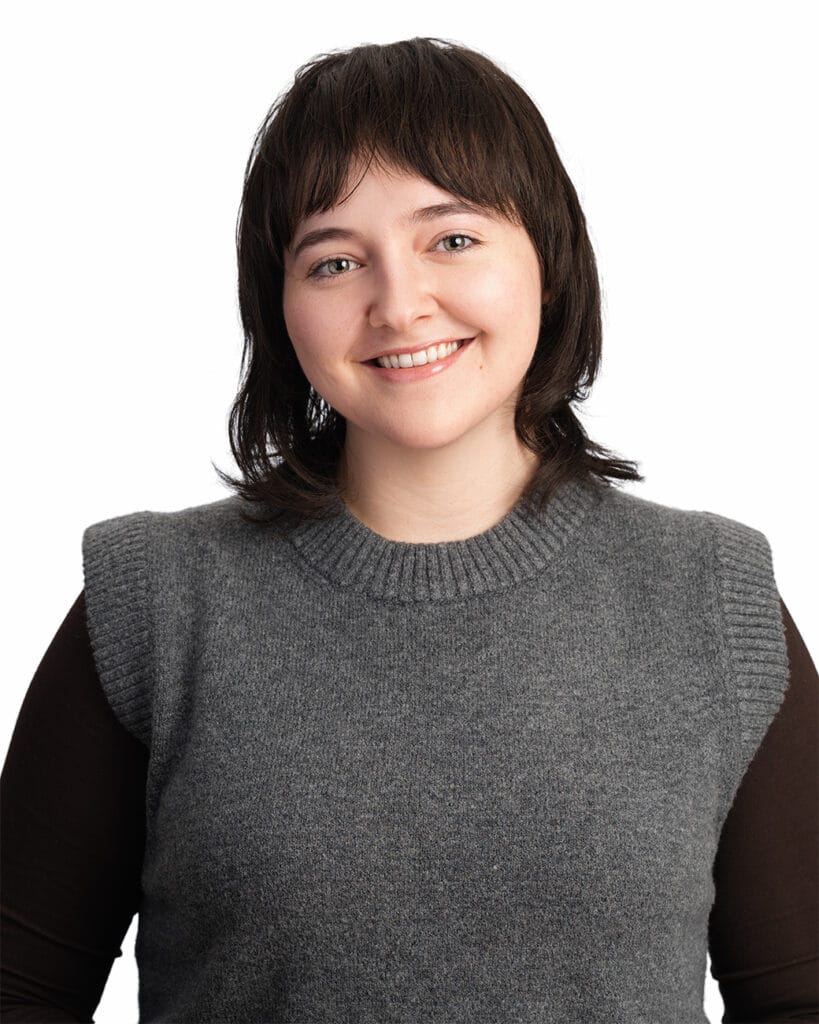 Brunette with gray sweater, brown sleeves, white backdrop, friendly smile, headshot, nyc photographer