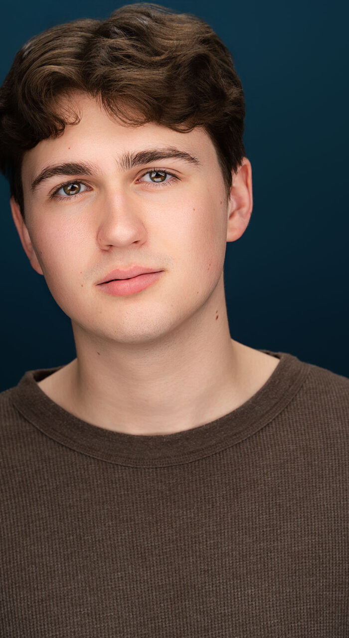 Actor headshot of Charlie Welch against a blue background